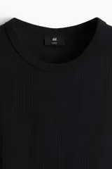Musculosa negra de punto acanalado, corte ajustado, cuello redondo y sisas con ribete fino.