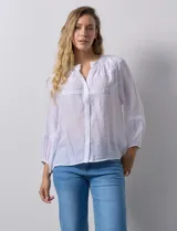 Blusa blanca de gasa bambula con cuello a la base y apertura central con botones. Apliques de crochet en la parte delantera y en las mangas ¾ con terminación fruncida.