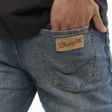 Pantalón jean Wrangler modelo Larston de corte slim fit, color azul con lavado medio y detalles de costuras en contraste. Cierre con cremallera y botón, cinco bolsillos y etiqueta de cuero con logo en la parte trasera.