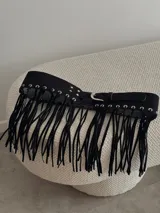 Cinturón ancho de gamuza color negro con hebilla plateada y flecos largos.