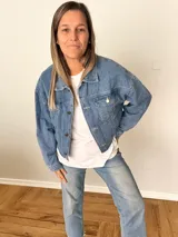 Campera de jean celeste con corte corto y fit relajado, botones metálicos frontales, bolsillos con solapa y espalda con elástico fruncido.