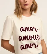 Remera color crema de algodón, corte slim, con cuello redondo y mangas cortas. Estampa frontal con las palabras 'amor', 'amour' y 'amore' en color borgoña.