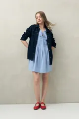 Vestido corto de lino color celeste claro, con escote con lazo ajustable y detalle de alforzas verticales en el frente.