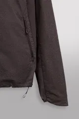 Cazadora marrón de tejido técnico ligero con partículas reflectantes. Tiene cuello alto con capucha elástica, mangas largas con puños elásticos, bolsillos frontales con cremallera en pecho y cadera, y cierre frontal con cremallera. Pertenece a la línea Zara Athleticz.