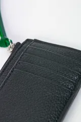 Tarjetero verde con capacidad para 4 tarjetas y bolsillo con cierre para objetos esenciales, con logo estampado en el frente.