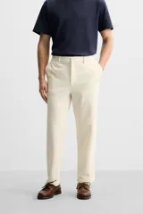 Pantalón color crudo de tejido con textura de rizo, corte relaxed fit, con cintura elástica, bolsillos frontales y traseros, cierre frontal con cremallera y botón.