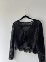 Top corto de encaje negro con mangas largas, escote en V y volados en el ruedo.