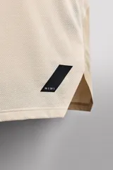 Camiseta deportiva sin mangas color beige, confeccionada en tejido técnico ligero y elástico con estructura perforada. Tiene cuello redondo amplio, sisas con acabados termofijados, bajo con aberturas laterales y logo estampado.