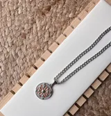 Cadena de acero quirúrgico con dije en forma de flor, adornado con detalles en color naranja.