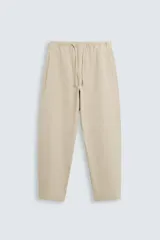 Pantalón color beige de corte carrot fit, confeccionado en tejido de algodón. Cuenta con cintura elástica ajustable con cordón, bolsillos frontales y bolsillo trasero de plastrón. Presenta un efecto lavado.