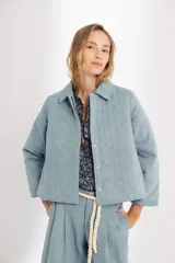 Chaqueta capitoneada celeste vintage de denim de algodón 100% natural pre-lavado y suavizado, con bolsillos laterales, botones a presión escondidos y ruedo curvo en los costados.