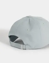 Gorra deportiva color crudo, de tela canvas con bordado frontal de la palabra "Wellness" en letras negras estilo universitario. Tiene visera curva y tira ajustable trasera con hebilla metálica.