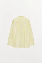 Camisa tipo pijamera a rayas amarillas y blancas, confeccionada en hilatura con algodón y lino. Tiene cuello solapa, manga larga con puños y cierre frontal con botones.