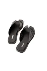 Sandalia plana negra de cuero blando con pala cruzada y aplique metálico decorativo.