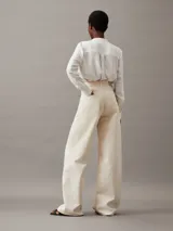 Blusa blanca de poliéster reciclado con escote en V, manga larga y detalle de pliegues en los hombros.