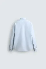 Camisa celeste de algodón con estructura twill, corte regular, cuello solapa, manga larga con puños abotonados y cierre frontal con botones.