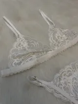 Conjunto de lencería blanco de encaje, compuesto por un bralette con breteles regulables y una tanga regulable con corte media less y entrepierna de algodón.