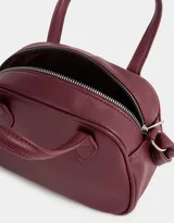 Cartera bowling color gris claro de cuerina con doble asa corta de mano, correa regulable y cierre superior.
