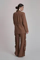 Blazer marrón con solapas de muesca, cierre frontal con lazo y mangas largas. Presenta volados a lo largo de las costuras laterales del pantalón a juego.