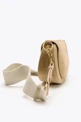 Bolso bandolera de gamuza color beige, con asa corta y correa larga extraíble. Cierre con solapa imantada y bolsillo interno con cierre.