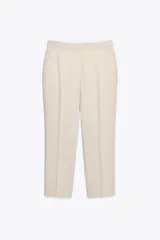 Pantalón negro tobillero de tiro alto con bolsillos delanteros y traseros. Tiene abertura lateral en el bajo y cierre frontal con cremallera y botón.