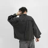 Chaqueta de jean negro con efecto lavado, corte recto, cuello clásico, cierre frontal con cremallera, bolsillos laterales y puños elásticos. Estampado con el texto "VENEFO COMPANY" en color naranja.