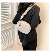 Cartera bandolera pequeña color beige, de cuero sintético con textura granulada. Tiene correa ancha de tela estampada con motivos geométricos y cierre superior con cremallera. Incluye un bolsillo frontal con cremallera y un dije metálico.