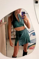 Falda corta de cuero ovino color verde azulado con efecto vintage, corte irregular y aberturas laterales con lazos.