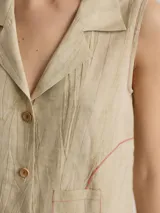 Camisa blanca sin mangas, con cuello camisero, cierre frontal con botones de madera y bolsillo de parche en el pecho.