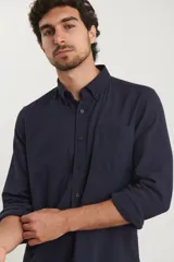 Camisa azul marino de lino y algodón, con cuello abotonado, manga larga con puños enrollados, bolsillo de parche en el pecho y cierre frontal con botones.
