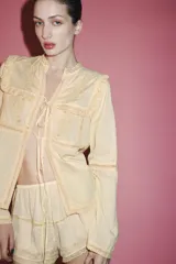 Blusa color crema de algodón y viscosa, con cuello mao y mangas largas. Presenta bordados florales con abalorios y terminaciones en puntilla. Se cierra con lazos en el frente.