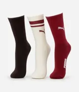 Kit de tres pares de medias deportivas Puma de caña larga. Un par color beige con dos rayas marrones horizontales en la parte superior y logo marrón en el tobillo. Un par color crema liso con logo blanco en el tobillo. Un par color marrón con una raya blanca horizontal en la parte superior y logo blanco en el tobillo.