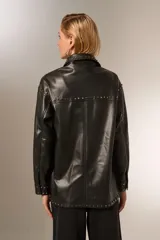 Chaqueta negra de eco-cuero con cuello camisero, corte holgado, cierre con broches y tachas plateadas.
