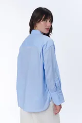 Camisa de manga larga de rayas azules y blancas, con bolsillos frontales y corte holgado.