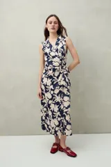 Vestido midi sin mangas con estampado floral y de hojas en tonos verde y marrón. Diseño cruzado tipo wrap con cuello sastrero y lazo ajustable en la cintura.