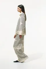 Pantalón de corte recto color crema con estampado geométrico en negro. Modelo de tiro alto con elástico en la parte posterior de la pretina y cierre oculto en un lateral.