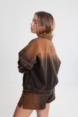 Campera de denim marrón con efecto degradado, corte boxy, cuello camisero, cierre frontal con botones metálicos, mangas largas con puños abotonados, dos bolsillos frontales con solapa y parche con logo en el frente.