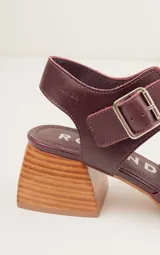 Sandalias negras de cuero con diseño minimalista y taco ancho geométrico en tono madera. La capellada lisa aporta una estética depurada y moderna, mientras que la pulsera con hebilla metálica ajustable asegura un calce firme y confortable.