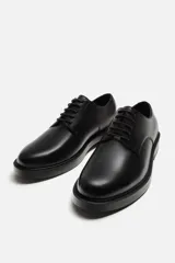 Zapato de vestir tipo derby de cuero negro, con puntera lisa, horma redonda y suela con ligero tacón.