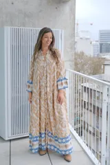 Vestido largo color beige con estampado abstracto en tonos marrones y azules, con cuello mao, mangas largas con puños elásticos y cierre frontal con botones.