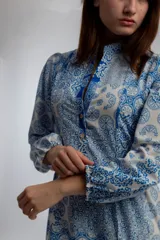Vestido midi de corte amplio con estampado floral en tonos azules y blancos. Tiene cuello mao con botones y mangas largas abullonadas.