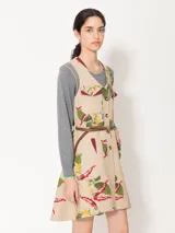 Vestido corto color beige con estampado floral, cuello en V, bolsillos frontales con solapa y botones dorados, y cinturón marrón de cuero vacuno con hebilla dorada.