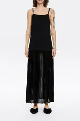 Vestido largo negro de punto con corte ajustado en la cadera y falda con vuelo, escote recto y tirantes dobles con aros metálicos y nudos.