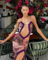 Vestido largo de corte ajustado, con estampado abstracto en tonos rosados y marrones. Presenta un escote pronunciado con detalle de volados en color púrpura, abertura en el abdomen y tajo lateral.