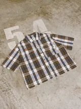 Camisa de manga corta con corte híbrido boxy fit/oversize, confeccionada en algodón. Disponible en tres diseños: a cuadros marrones, a rayas blancas y negras, y a rayas burdeos y blancas. Presenta bordados de diseño propio de la marca.