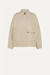 Chaqueta corta color beige, de cuello estilo camisa, con cierre de botones oculto, mangas murciélago y bolsillos con solapa.