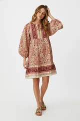Vestido corto de algodón con estampado floral en tonos beige, naranja y borgoña. Tiene cuello redondo con lazo ajustable, mangas largas abullonadas y corte holgado.