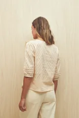 Blusa color crema con diseño calado, escote en V y volados frontales. Tiene mangas 3/4 con puños elastizados y cierre frontal con botones.