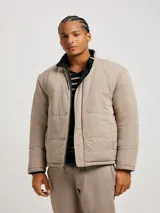 Campera acolchada reversible, color negro con interior beige, cuello mao y cierre frontal con cremallera.