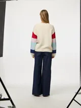Sweater de punto color crema con cuello redondo y mangas largas con rayas horizontales en colores rojo, celeste, azul y rosa.